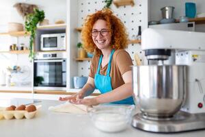 feliz atraente jovem adulto mulher dona de casa padeiro vestem avental segurando PIN rolando massa em cozinha mesa cozimento pastelaria conceito cozinhando bolo bolacha fazendo padaria fazer caseiro pizza às casa foto