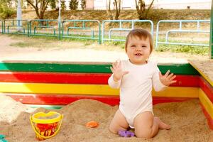 bebê menina jogando dentro a caixa de areia em a Parque infantil em uma verão ensolarado dia foto