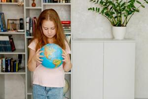 fofa menina cuidadosamente examina a globo contra a fundo do uma estante de livros foto