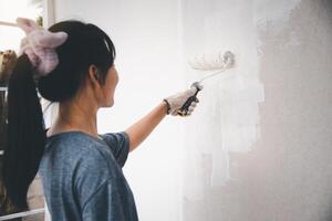 jovem mulher pintura a paredes com uma rolo usando branco pintar. foto