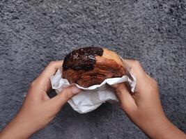 mãos segurando cromboloni, volta croissant, Novo Iorque rolar, uma viral pastelaria combinando croissants e bomboloni em concreto parede fundo. foto