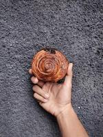 mão segurando cromboloni, volta croissant, Novo Iorque rolar, uma viral pastelaria combinando croissants e bomboloni em concreto parede fundo. foto