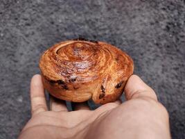 mão segurando cromboloni, volta croissant, Novo Iorque rolar, uma viral pastelaria combinando croissants e bomboloni em concreto parede fundo. foto