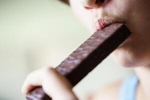 colheita anônimo jovem menina comendo chocolate proteína Barra foto