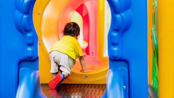 ásia feliz crianças desfrutando hora de brincar às a Parque infantil com sorrisos e riso em uma ensolarado verão dia. atrás bebê Garoto quem estava escalada em a jogar equipamento, criança estava rastejando para dentro a brinquedo túnel. foto