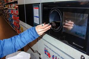 nitra, Eslováquia - 16.01.2024 fechar-se do uma do homem mão colocando uma garrafa para dentro uma desperdício reciclando máquina. foto