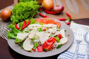 picante vidro macarrão salada com vietnamita linguiça servido dentro uma cinzento prato colocar em uma de madeira mesa e vários legumes. foto