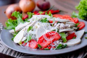 picante vidro macarrão salada com vietnamita linguiça servido dentro uma cinzento prato colocar em uma de madeira mesa e vários legumes. foto