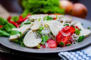 picante vidro macarrão salada com vietnamita linguiça servido dentro uma cinzento prato colocar em uma de madeira mesa e vários legumes. foto