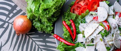 picante vidro macarrão salada com vietnamita linguiça servido dentro uma cinzento prato colocar em uma de madeira mesa e vários legumes. foto