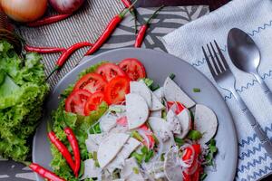 picante vidro macarrão salada com vietnamita linguiça servido dentro uma cinzento prato colocar em uma de madeira mesa e vários legumes. foto