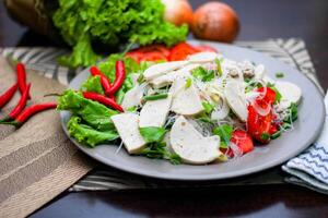 picante vidro macarrão salada com vietnamita linguiça servido dentro uma cinzento prato colocar em uma de madeira mesa e vários legumes. foto