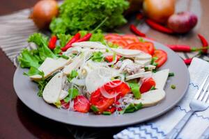 picante vidro macarrão salada com vietnamita linguiça servido dentro uma cinzento prato colocar em uma de madeira mesa e vários legumes. foto