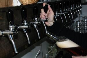 atrás a contador. mulheres mãos belas e facilmente derramar Cerveja para dentro uma garrafa. foto