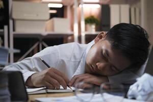jovem cansado homem de negocios deitado em mesa às noite escritório. foto