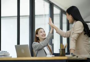 dois mulheres estão cumprimentando com alegria às seus sucesso dentro negócios. e comemoro desempenho e trabalho em equipe. foto