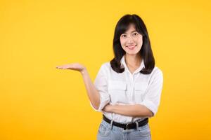 feliz jovem ásia mulher vestindo branco camisa e jeans brim plantas apresentando ou mostrando aberto mão Palma com cópia de espaço para produtos isolado em amarelo fundo. presente produtos publicidade conceito. foto