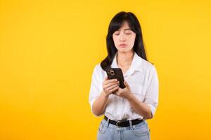 retrato fêmea ansioso assustado em a telefone vendo mau notícias, jovem lindo ásia mulher vestindo branco camisa e jeans plantas chocado com Móvel telefone isolado em amarelo fundo. mau notícia conceito. foto