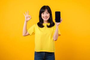 positivo retrato jovem ásia mulher vestindo amarelo camiseta e jeans jeans mostrando feliz sorrir enquanto mostrando Smartphone tela e fazer a OK mão placa gesto. recomendado formulários conceito. foto