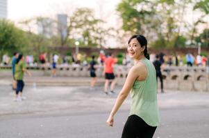 fêmea corredor. em forma jovem ásia mulher com verde roupa de esporte aeróbica dança exercício dentro parque e desfrutando uma saudável ar livre. ginástica corredor menina dentro público parque. bem estar ser conceito foto