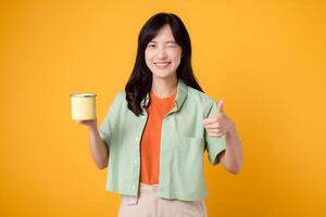 positividade alegre retrato. jovem ásia mulher vestem verde camisa em laranja camisa mostrar feliz sorrir enquanto segurando copo do café e dando polegar acima gesto. delicioso momento e espalhando positividade. foto