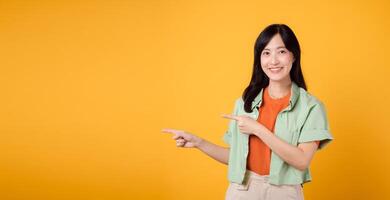 jovem ásia mulher dentro dela 30s vestindo uma verde camisa em a laranja camisa, apontando dedos para livre cópia de espaço. explorar a conceito do desconto compras promoção foto