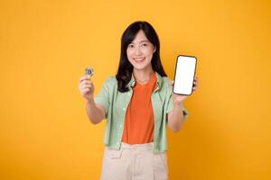 a inovação do futuro finança com jovem ásia mulher dentro dela 30s, elegantemente vestido dentro laranja camisa e verde saltador, usando Smartphone tela exibição e criptografia moeda moeda em amarelo fundo. foto