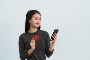 ásia mulher segurando mostrando crédito cartão e Móvel telefone para compras conectados isolado em branco ou cinzento fundo estúdio. conectados compras, comércio eletrônico, Internet bancário, gastos dinheiro conceito. foto