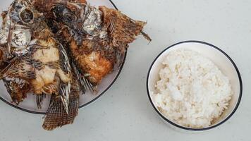 branco arroz dentro uma tigela e frito peixe em uma branco prato estão servido em a mesa foto