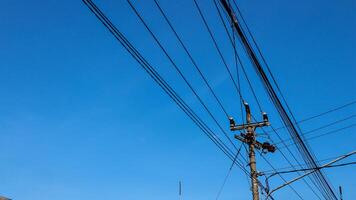 elétrico fios e elétrico postes cruzando a Alto Voltagem pólo torre contra a azul céu fundo. foto