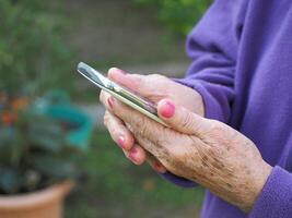 fechar-se do idosos mulher mãos segurando Móvel telefone. foto