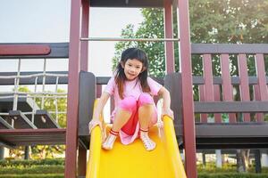 fofa ásia menina jogando em a deslizar dentro a Parque infantil foto