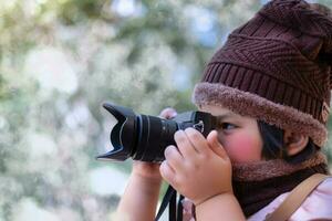 retrato de uma menina bonitinha com chapéu de lã tirando uma foto com a câmera digital no clima está frio no fundo desfocado