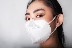 close-up de uma jovem mulher asiática colocando uma máscara médica n95 para se proteger de doenças respiratórias transmitidas pelo ar como a gripe covid-19 pm2.5 poeira e poluição em fundo cinza, conceito de infecção de vírus de segurança foto