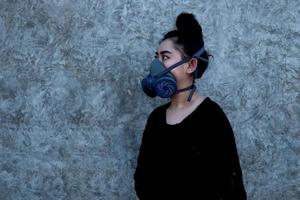 retrato jovem ásia vestindo um respirador de filtro de partículas substituível de meia máscara no fundo da parede de concreto com espaço de cópia foto