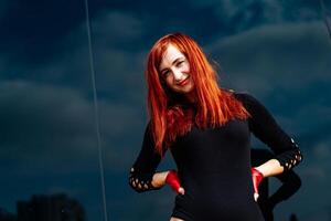 mulher com vermelho cabelo dentro Preto vestir de pé. uma mulher com vermelho cabelo em pé com confiança vestindo uma Preto vestir. foto