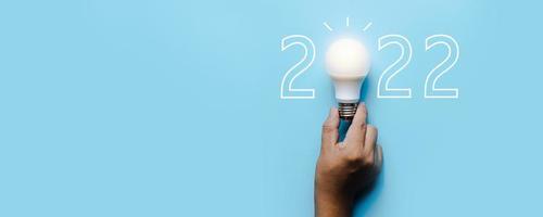 ideia e criatividade em 2022, lâmpada com número de ano novo em fundo azul foto