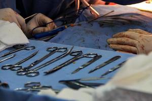 mesa de instrumentos cirúrgicos e, ao fundo, os médicos realizando a cirurgia