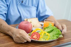 paciente asiático sênior ou idosa idosa comendo alimentos saudáveis de vegetais de café da manhã com esperança e feliz enquanto está sentado e com fome na cama no hospital. foto