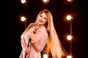 Jovem sorridente linda garota de cabelo comprido com microfone cantando no palco no karaokê foto