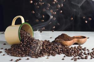 xícara de café e grãos para espalhar e café moído em uma tigela de madeira sobre um fundo branco foto