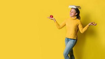 uma garota com um livro na cabeça e uma maçã vermelha na mão enquanto fazia ioga em fundo amarelo. o conceito de exercício para uma boa saúde. amante da saúde foto