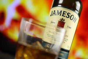 Kyiv, Ucrânia - pode 4, 2022 Jameson original álcool garrafa em de madeira mesa com vermelho lareira foto
