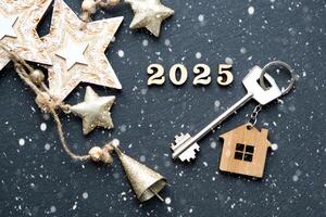 casa chave com chaveiro chalé em festivo Preto fundo com estrelas, luzes do guirlandas. Novo ano 2025 de madeira cartas, cumprimento cartão. comprar, construção, realocação, hipoteca, seguro foto