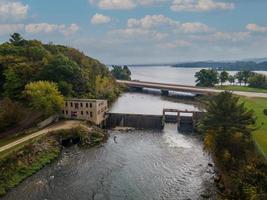 vista aérea da represa com ponte sobre o rio e o lago no outono, casa do leme histórica com estrada de cascalho, vertedouro ativo foto
