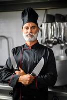 confiante chefe de cozinha posando com facas dentro cozinha foto