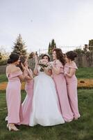 grupo retrato do a noiva e damas de honra. noiva dentro uma Casamento vestir e damas de honra dentro Rosa ou pó vestidos e segurando à moda buquês em a Casamento dia. foto