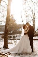 inverno casamento. uma feliz casal dentro Casamento roupas estão abraçando e sorridente dentro uma inverno parque coberto com neve em seus Casamento dia. inverno amor história do uma lindo casal dentro Nevado inverno clima foto