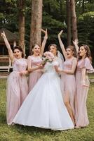 grupo retrato do a noiva e damas de honra. noiva dentro uma Casamento vestir e damas de honra dentro Rosa ou pó vestidos e segurando à moda buquês em a Casamento dia. foto