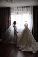 uma feliz noiva é preparando para dela luxuoso Casamento dentro uma hotel sala, com uma Casamento vestir em uma manequim próximo. retrato do uma mulher com elegante cabelo, Maquiagem e uma sorrir dentro uma vestir vestido. foto